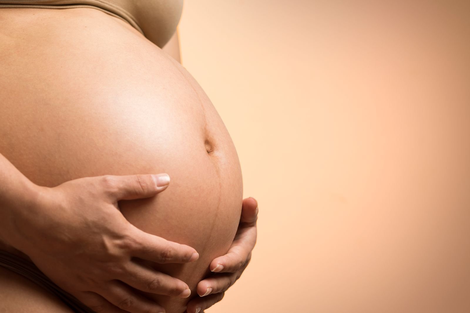 Mani che accarezzano il pancione in gravidanza, luce calda